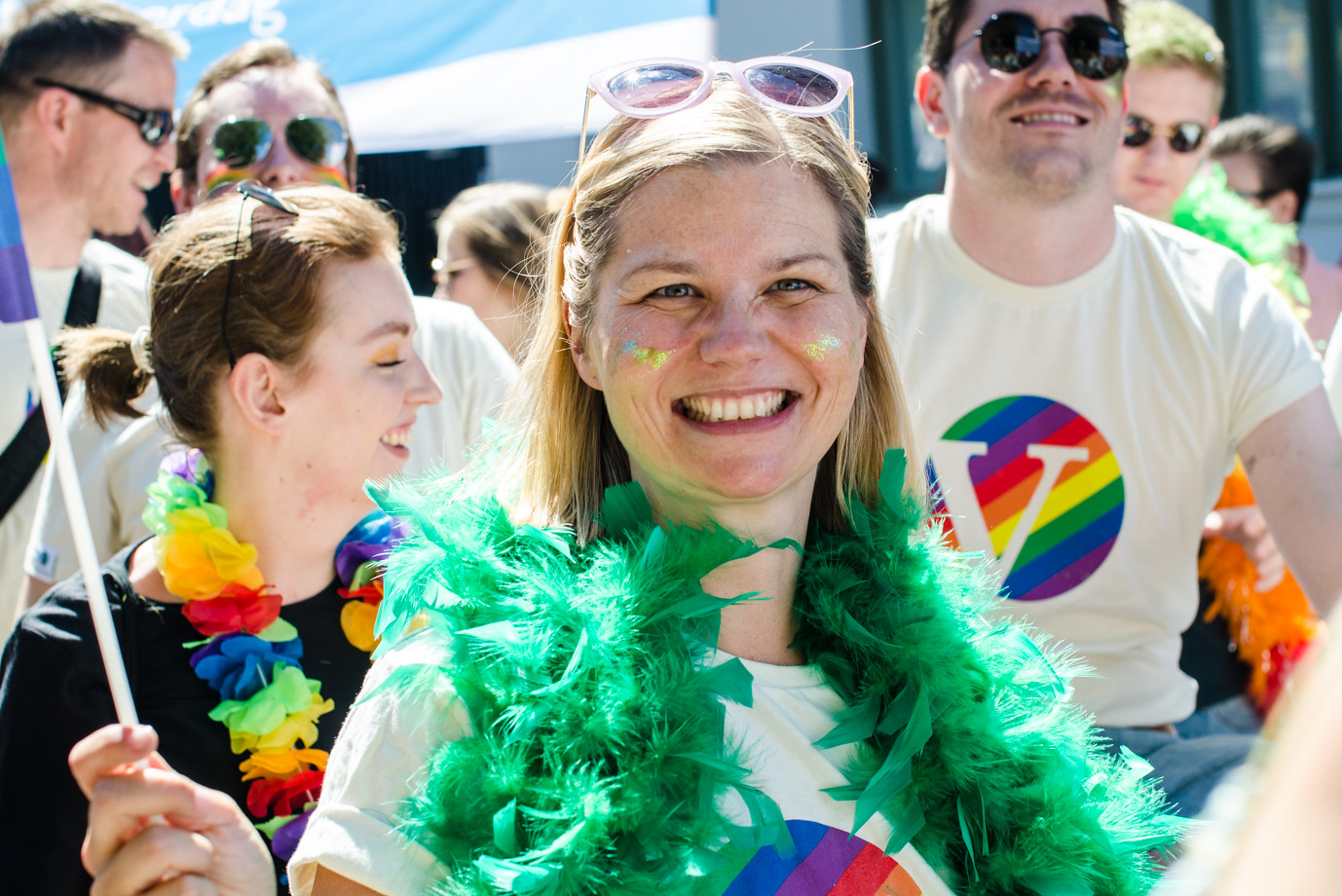 Tre representanter fra Venstre på Pride: Guri Melby står midt i bildet og smiler bredt, iført en t-skjorte i Venstres logo i pride-farger. Bak til høyre står Grunde Almeland i regnbuefarget venstre-tskjorte, og til høyre Anna Dåsnes