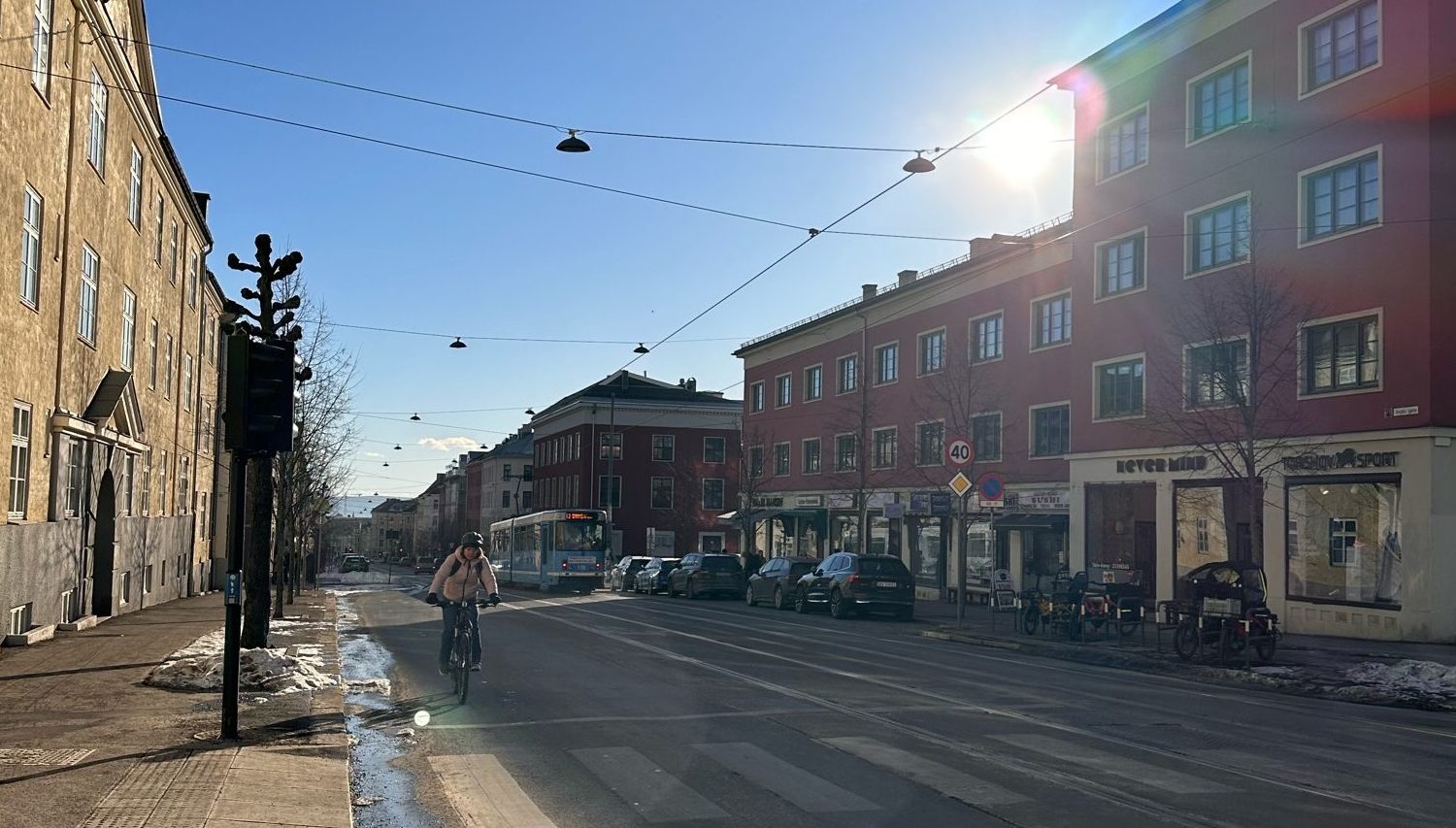 Bilde av bygate i vårsol med trikkeskinner, trikk og syklende person