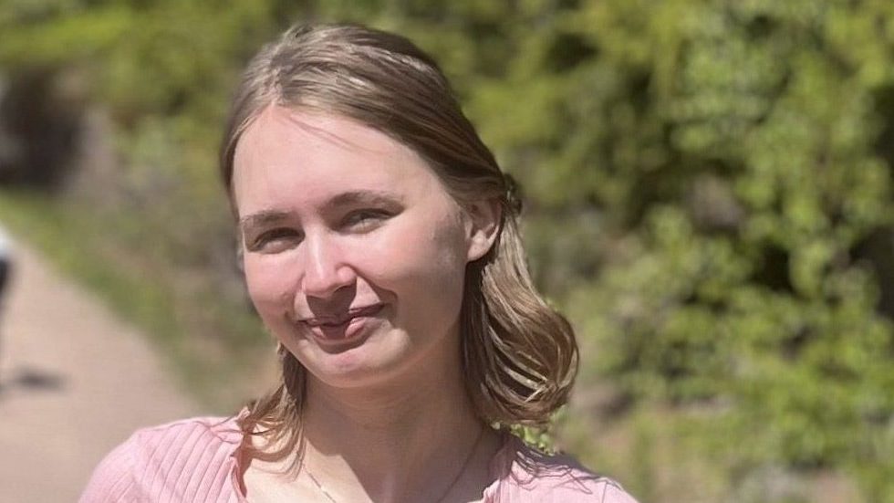 Emilie Ovnerud myser mot solen i en rosa tskjorte med skog i bakgrunnen