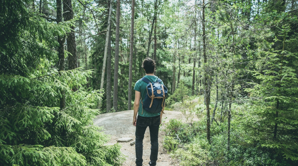 Bilde av mann som staar med ryggsekk paa en sti i skogen.