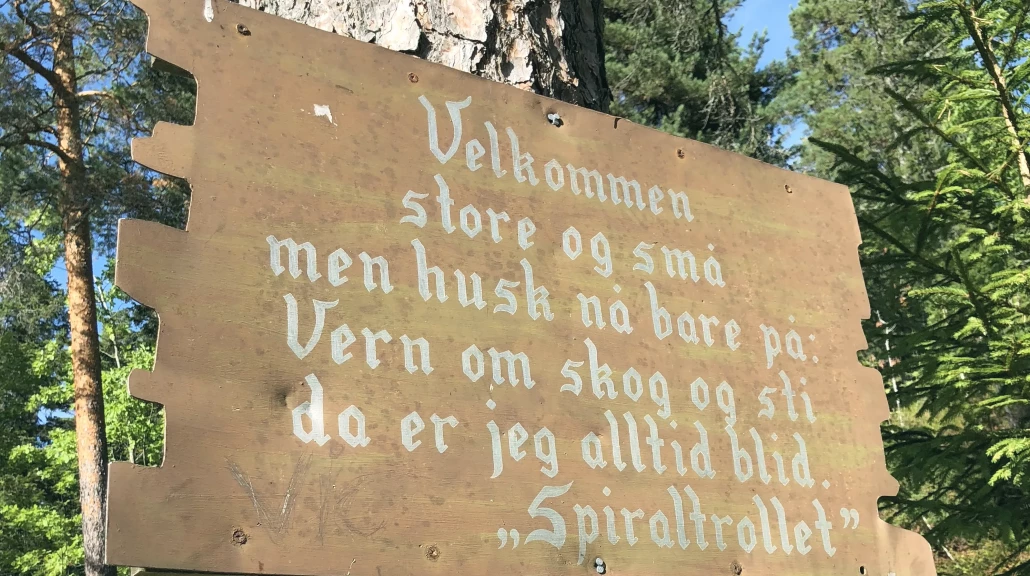Brunt treskilt festet paa et tre med tekst fra Spiraltrollet i Drammen.