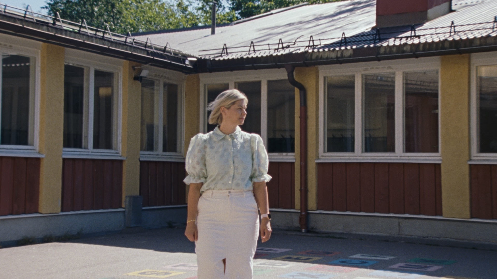 Guri Melby står i en åpen skolegård iført en lys dressjakke, med et alvorlig uttrykk, mens hun taler om alvoret i norsk politikk og viktigheten av europeisk samarbeid.
