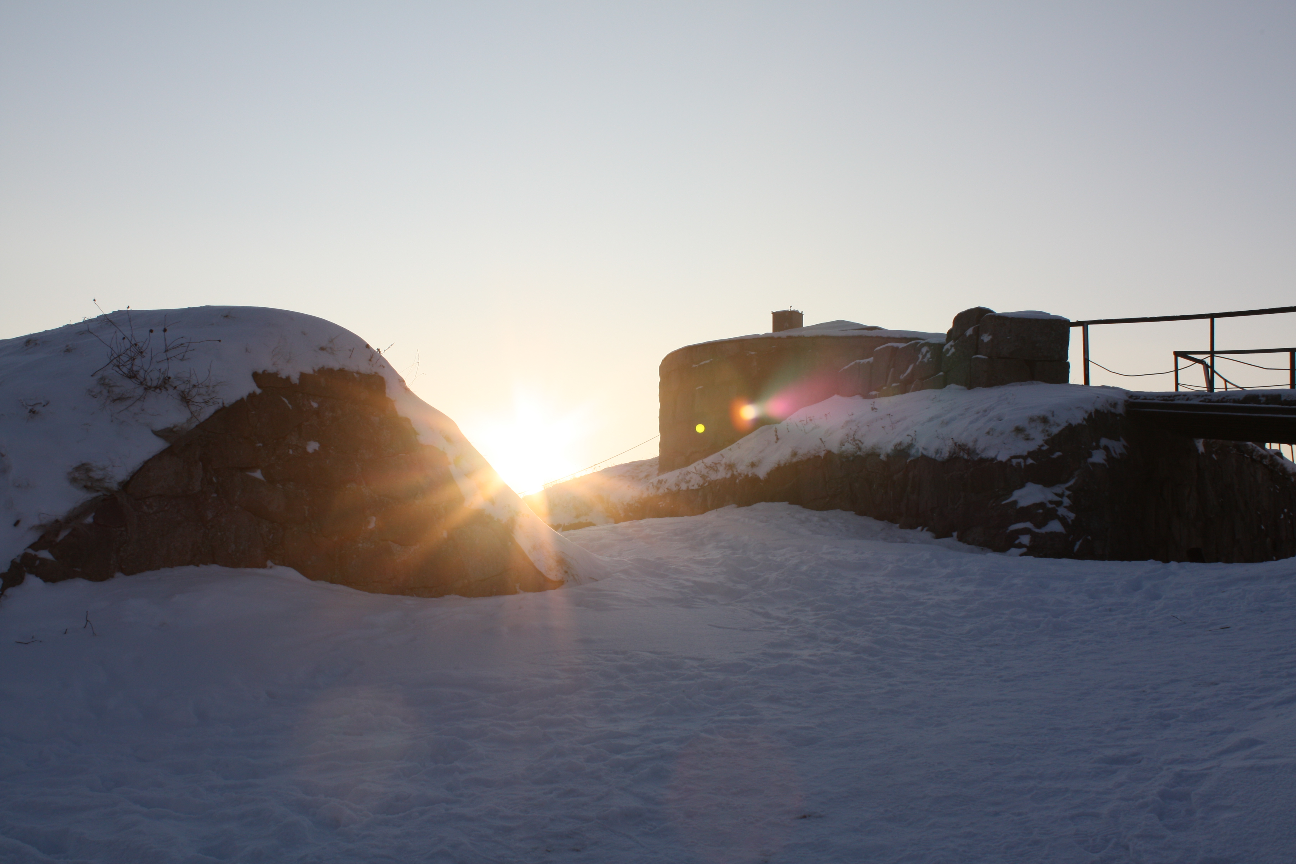 Solen stikker frem over Fredriksten festning en vintermorgen. Festningen er dekket av snø.