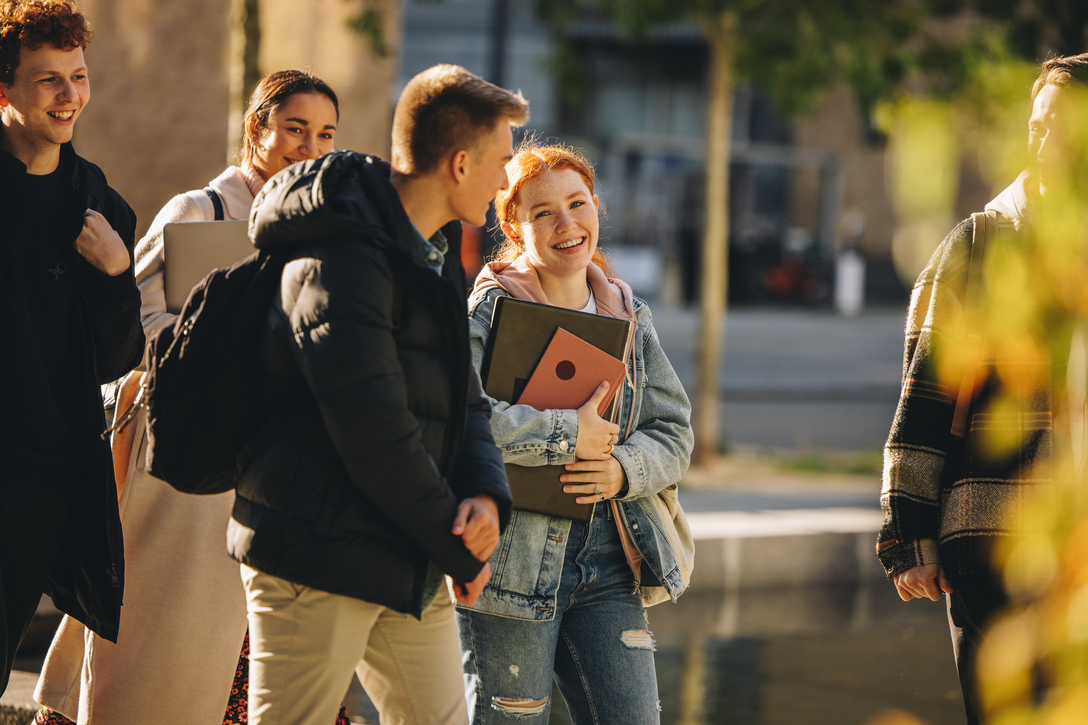 Smilende student går sammen med medstudenter utendørs på universitetsområdet etter forelesning.