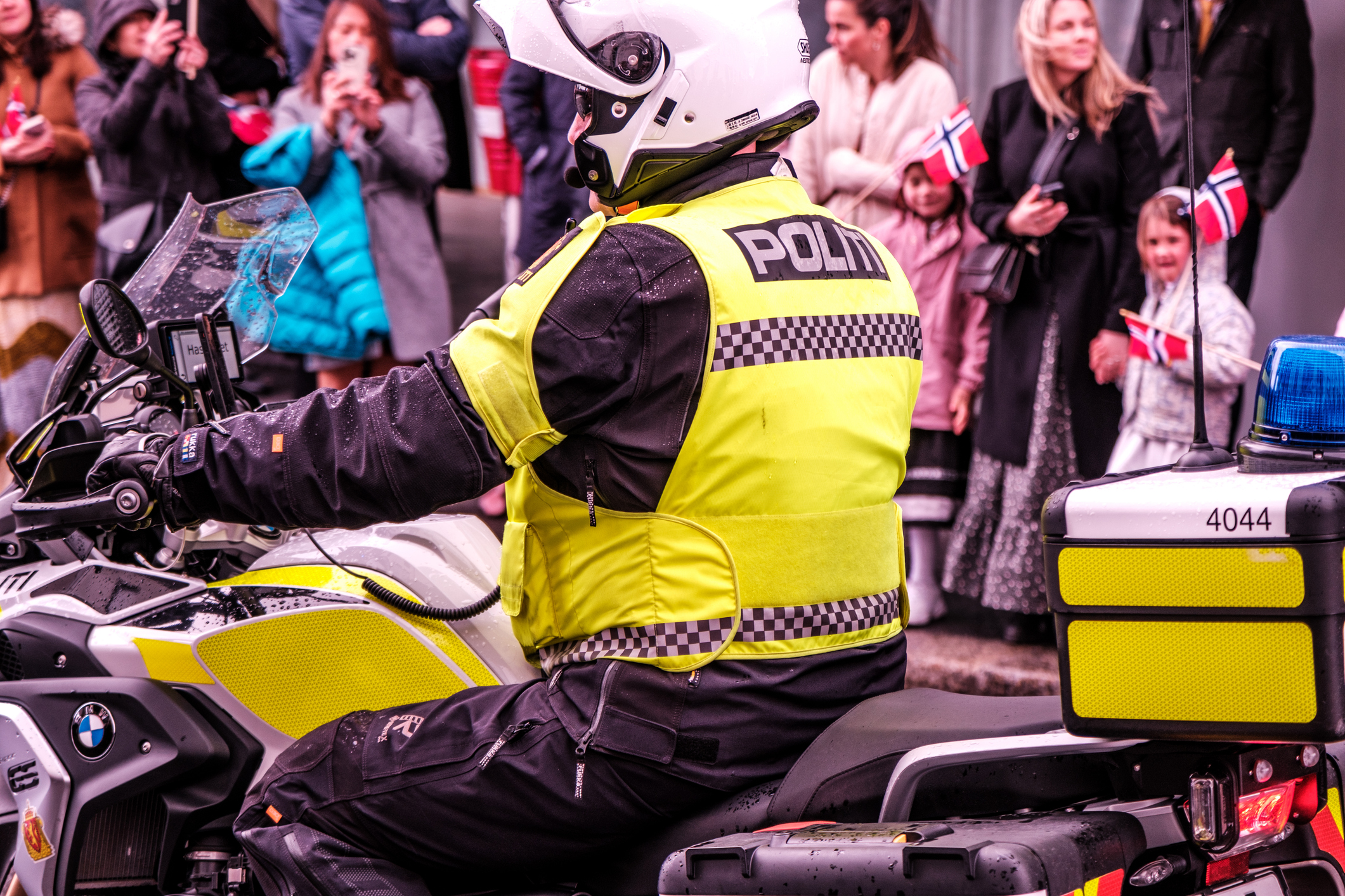 Norsk politibetjent på motorsykkel under 17. mai-feiring i Sandnes, omgitt av folk og flagg.
