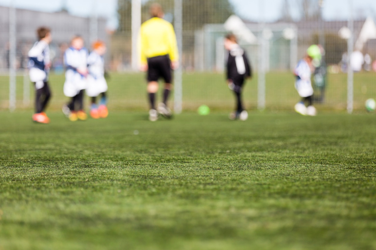 Uskarpt bilde av barn som spiller fotballkamp utendørs på en grønn bane – en aktiv scene fra barneidrett.