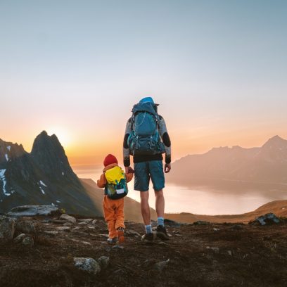 naturbilde: En far og hans barn står på toppen av et fjell i norsk natur, kledd for fjelltur, og ser utover landskapet med en vakker solnedgang i horisonten. Bildet symboliserer Venstres klima- og miljøpolitikk, med fokus på bærekraft og framtidige generasjoner.
