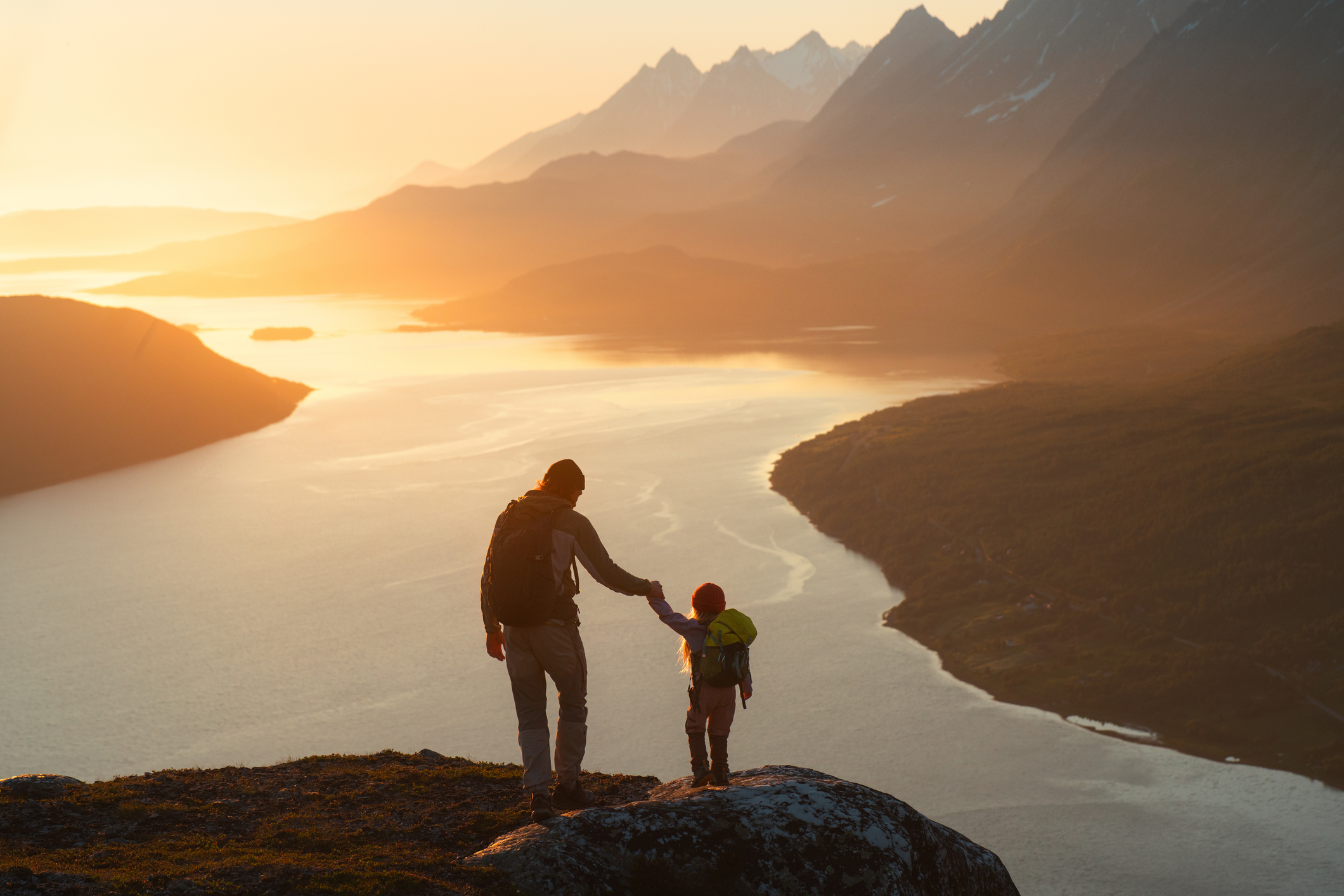 Far og barn på fottur i norsk fjellnatur ved solnedgang – symbol på hvordan Oljefondet skal sikre verdier og muligheter for framtidige generasjoner.