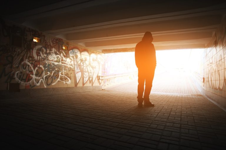 En person i hettegenser står alene i en mørk undergang med graffitivegger, vendt mot et sterkt lys i enden av tunnelen. Bildet symboliserer håp og veien ut av mørket for mennesker som sliter med rus og psykisk sykdom.
