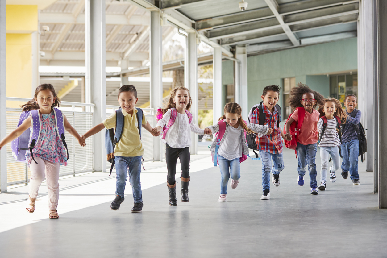 Bilde av barn på en skole som holder hender og løper smilende gjennom en gang på skolen.