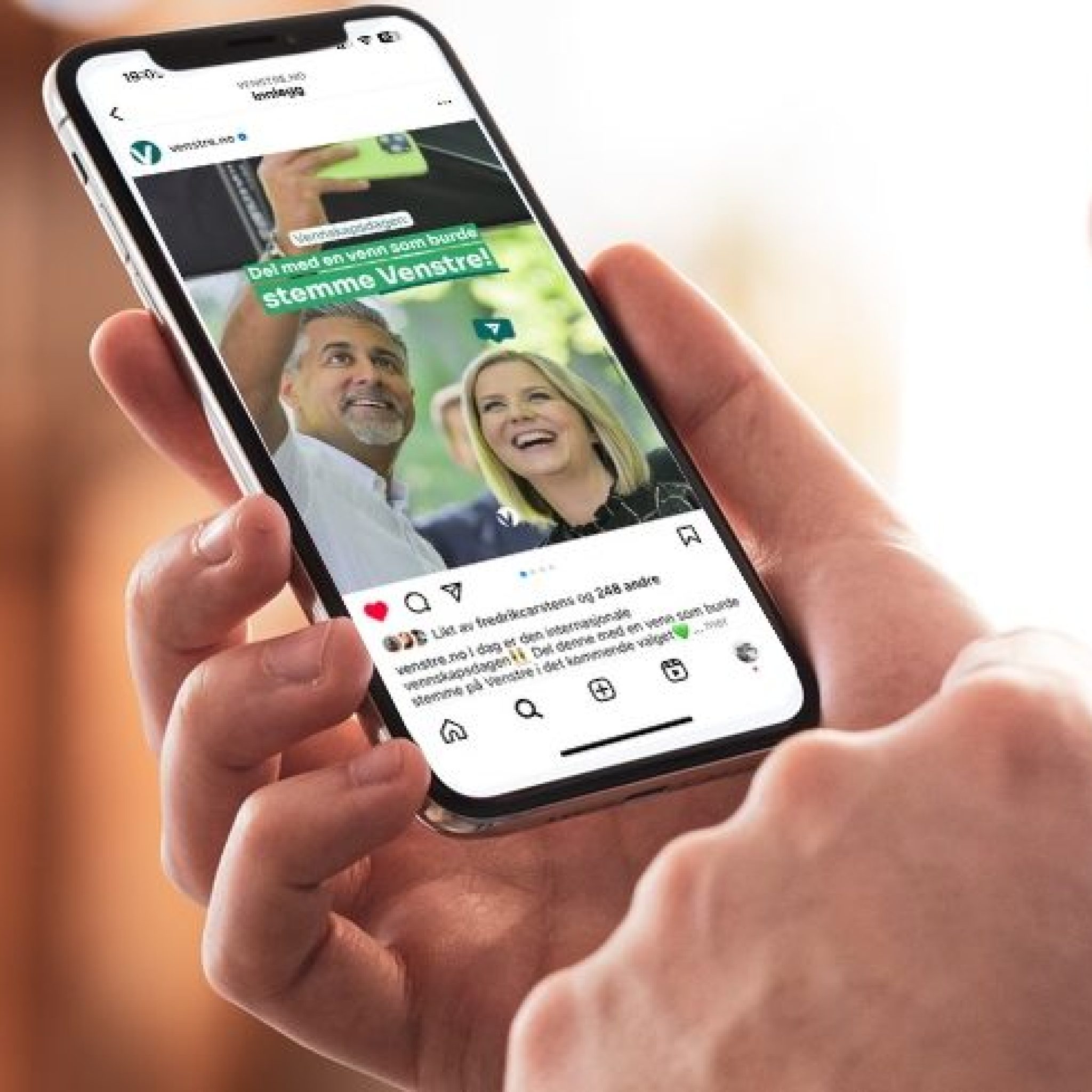 Nærbilde av to hender som holder en iPhone, med skjermen i fokus. På skjermen vises Venstres Instagram-profil med profilbilde, innleggsgalleri og «Følg»-knapp.