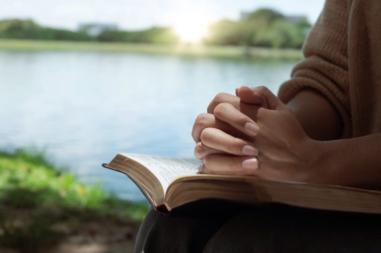 Kvinnehender foldet i bønn over en bibel i fanget – et stille øyeblikk som uttrykker tro og livssyn i naturen